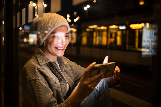 Woman smiling while checking mobile device in a colorful city at night