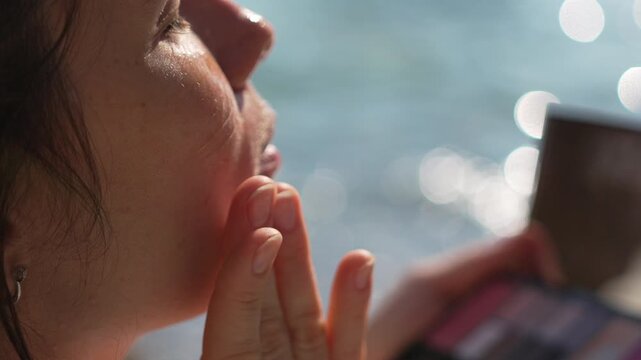 Makeup application woman beach young woman applies face cream while sitting by the sparkling sea in bright sunlight