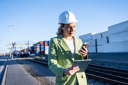 Logistics manager using smartphone and tablet at cargo port