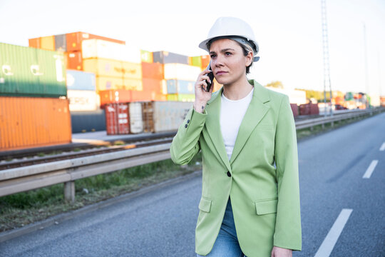 Businesswoman in helmet talking on smartphone at logistics port
