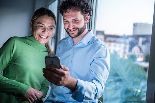 Smiling colleagues reading a message on a mobile device in the office