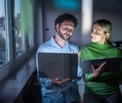 Business partners working overtime with notebook and tablet at night