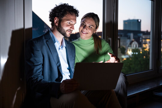 Colleagues work on a laptop by the window in the evening