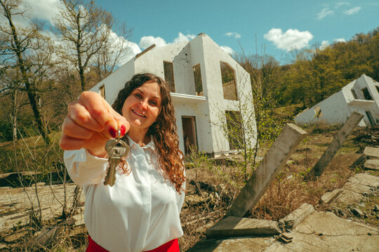 Realtor holding key to a destroyed house outdoors with humor