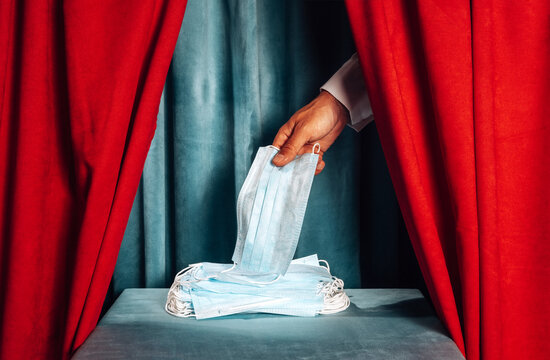 Hand from theater curtain holding medical mask on stage