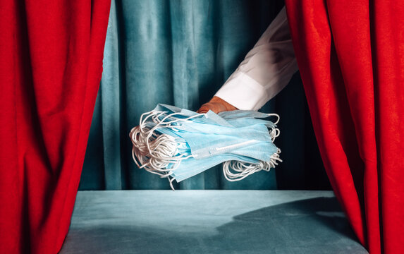 Hand holding medical masks behind a red theater curtain