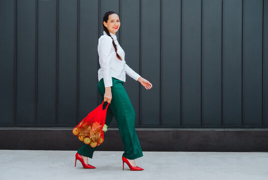 Smiling woman walking outdoors carrying net bag with fruit