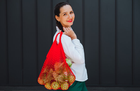 Smiling shopper holding reusable net bag with fresh green apples