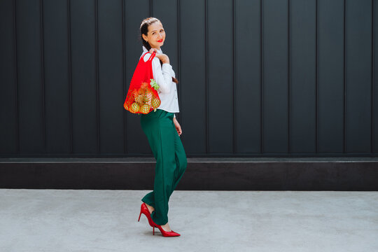 Smiling shopper walking outdoors with eco friendly net bag of fruit