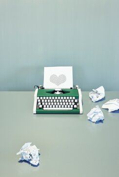 Green retro typewriter with binary heart shape and crumpled paper