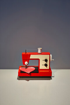 Red vintage sewing machine repairing a broken pink heart indoors