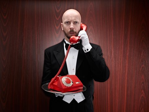 Butler holding a red retro telephone on a silver tray indoors