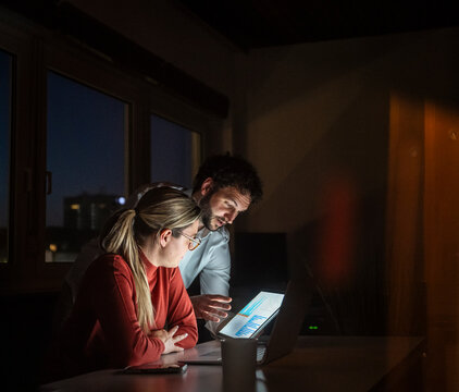 Business colleagues analyzing chart on notebook at night in office