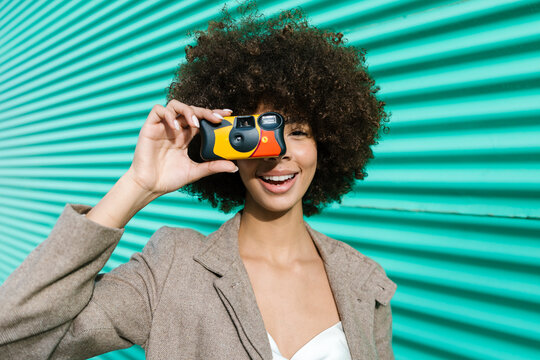 Cheerful woman with afro holding colorful camera outdoors