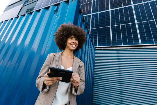 Cheerful female manager holds tablet near solar panel container