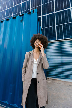 Smiling businesswoman on smartphone near solar panel and container