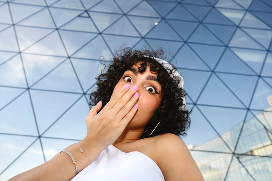 Surprised woman covering mouth outdoors by modern architecture