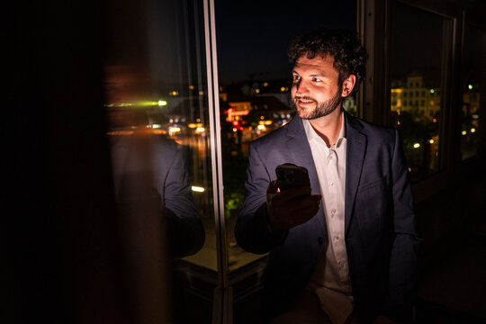 Executive holding smartphone looking out office window at night
