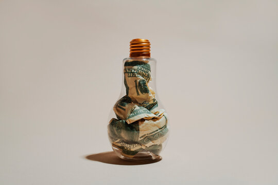 Transparent lightbulb filled with crumpled dollar bank notes