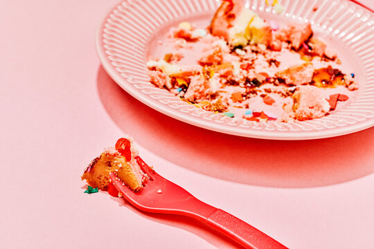 Last bite of cake on a red fork near a messy pink plate