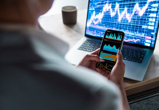 Trader analyzing stock market data on smartphone and laptop in office