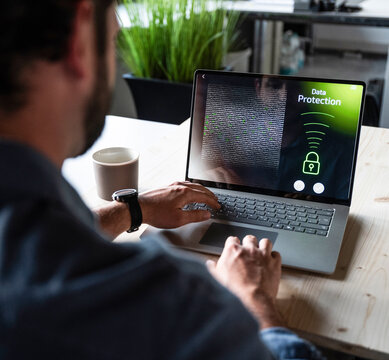 Programmer typing on laptop with data protection screen in office