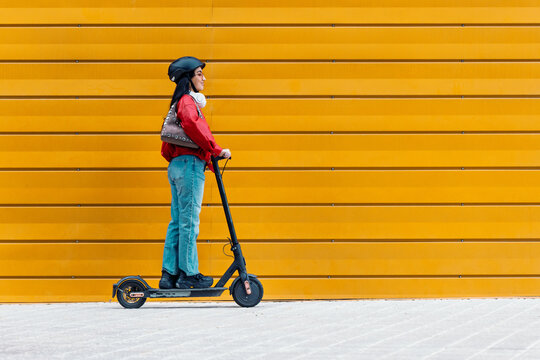 Woman riding electric scooter along yellow wall
