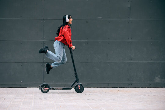 Woman jumping on electric scooter while listening to music