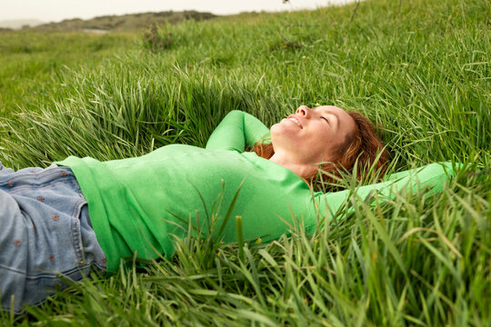 Happy woman lying in green grass relaxing in a meadow in Spain