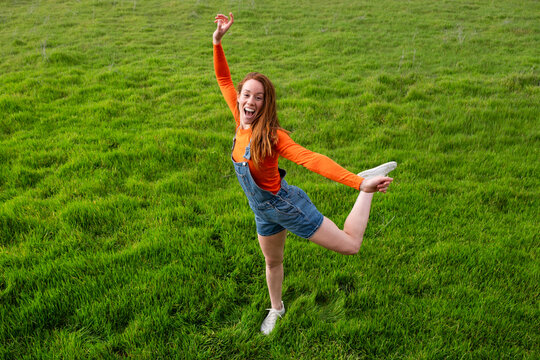 Happy model in orange shirt balancing on grass field in Granada
