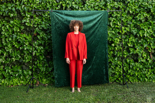 Barefoot fashion model in red suit posing outdoors in garden