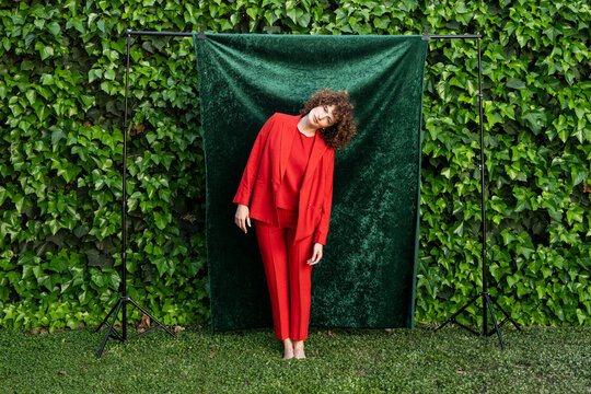 Fashion model posing outdoors in orange suit by a green backdrop