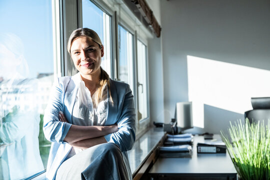 Smiling businesswoman sitting on windowsill at the modern office