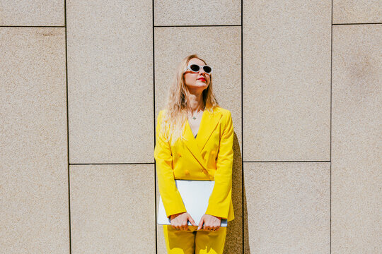 Happy freelancer wearing yellow suit holding laptop outside