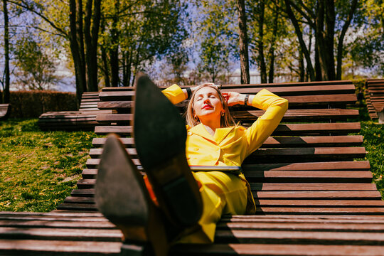 Happy freelancer in yellow suit resting on bench with laptop