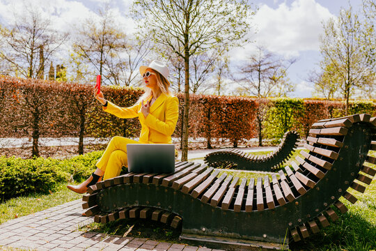 Happy freelancer in yellow suit using phone on park bench