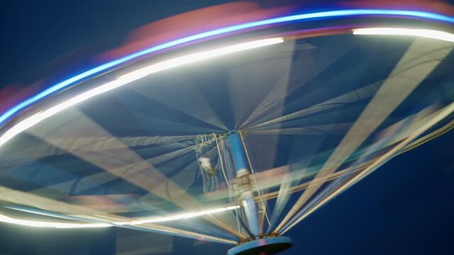 Empty chain swing ride lit with bright LED lights during evening twilight. 4K.