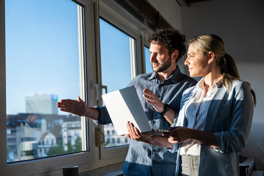 Business team brainstorming with laptop by office window
