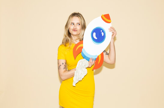 Model in yellow dress holding paper rocket symbolizing ambition