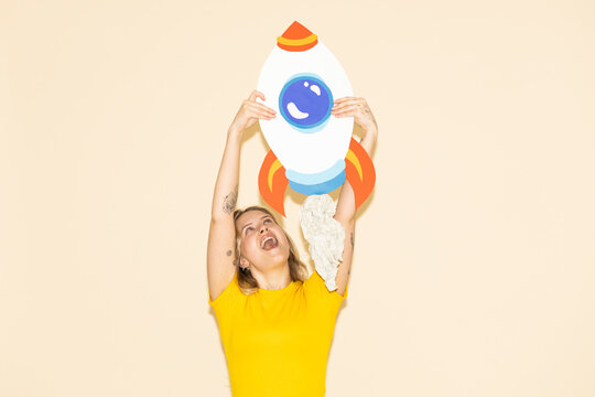 Excited entrepreneur in yellow holding a paper rocket for success
