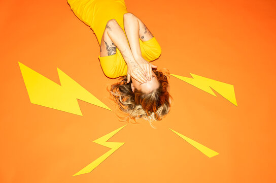 Hiding face surrounded by paper lightning bolts on orange