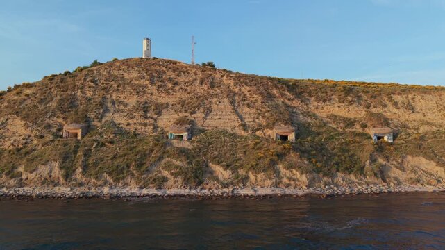 Aerial view of concrete military bunkers built into a coastal hillside with a lighthouse on the summit overlooking the Adriatic Sea in Zvernec, Vlore County, Albania.