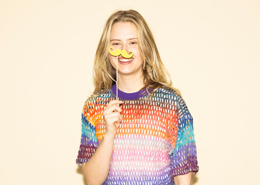 Woman smiling and holding a paper moustache in a multi coloured sweater