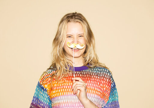 Smiling woman with a fake paper mustache prop on a beige background