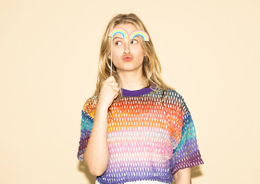 Woman holding rainbow paper prop wearing multi colored sweater for pride