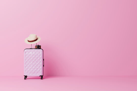 Pink suitcase with hat and vintage camera on pink background