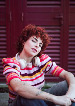Retro redhead with headphone and tattoo sitting outdoors