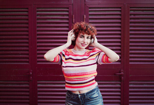 Smiling redhead listens to music with headphones outdoors