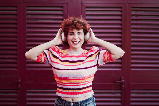 Redhead smiling and listening to music with headphone outdoors