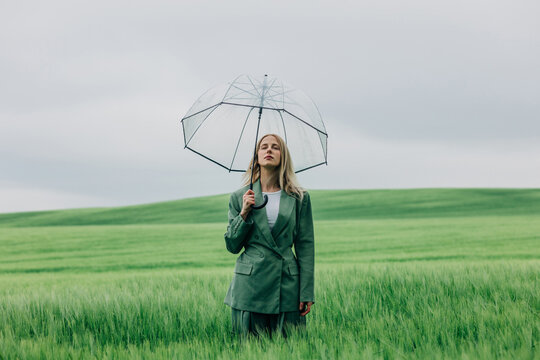 Businesswoman with clear umbrella standing in green wheat field